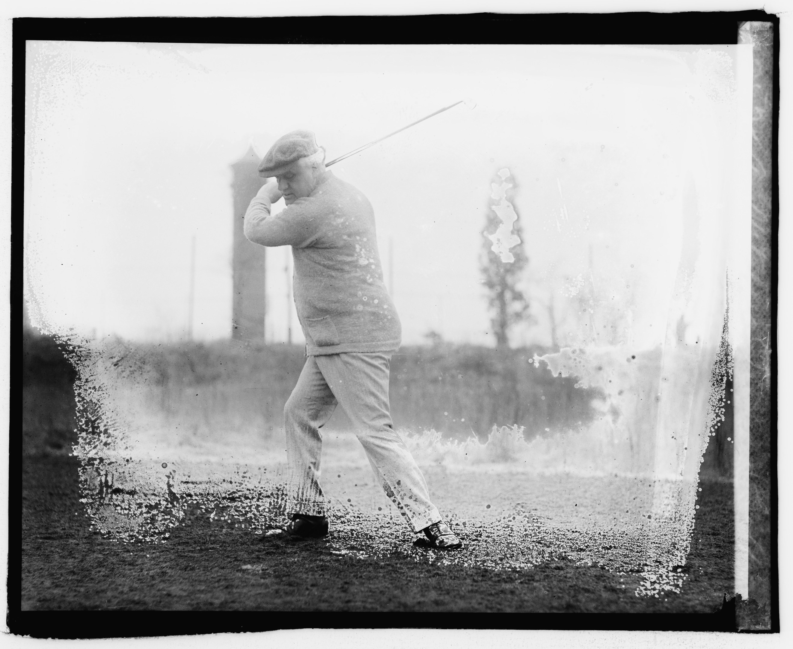 Schwarz-weiß-Foto eines Mannes, der einen Golfschläger auf einem grasbewachsenen Gebiet schwingt.