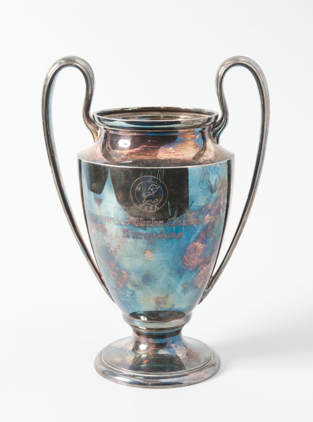 Der UEFA Champions League Pokal, ein stählerner Becher mit zwei Griffen und einem blauen und silbernen Farbschema, mit der Inschrift "UEFA Champions League", vor einem weißen Hintergrund dargestellt.