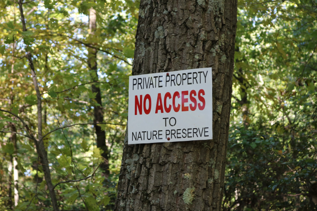 Ein Baum mit einem "Privatgrundstück - Kein Zugang zum Naturreservat" Schild auf seinem Stamm, umgeben von dichtem Wald im Hintergrund.