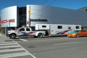 Ein Polizei-Lkw vor einem Gebäude mit Text, eine Ampel mit Stange und Drähten im Vordergrund und Bäume mit klarem blauem Himmel im Hintergrund.