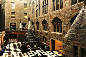 Großer Raum mit schwarz-weißem Schachbrettboden, Treppe, Geländern, Fenstern, Lampen und Menschen an Tischen und Stühlen, Teil einer Harry-Potter-Studio-Tour in London.