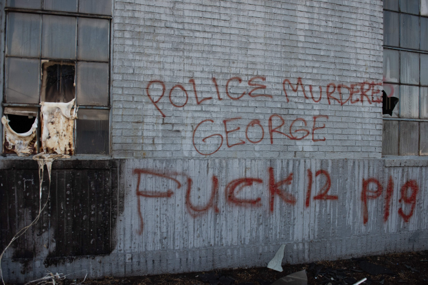 Graffiti an einer Gebäudewand mit der Aufschrift "Polizei Mord George Fuck 12 P19" mit Fenstern und verstreuten Gegenständen davor.