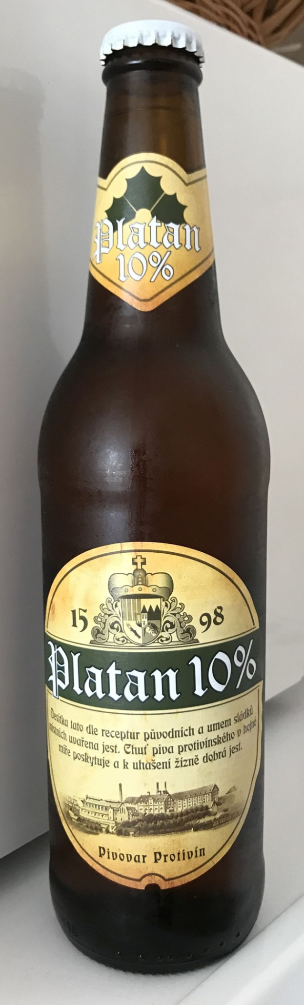 Eine Flasche Platan 10% Bier auf einem weißen Tisch mit einem Korb im Hintergrund.