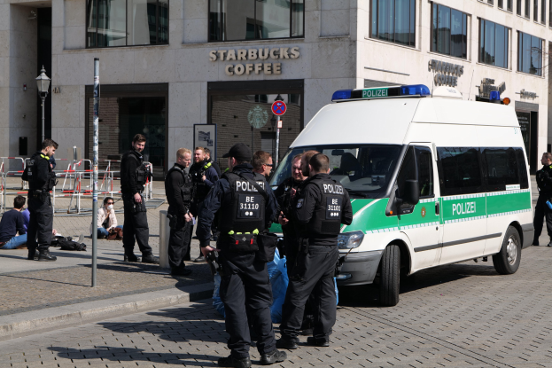 Polizeibeamte vor einem Starbucks-Café mit einem Van auf der rechten Seite und Menschen auf der linken Seite, mit einem Gebäude, einem Schild, einem Laternenmast und einer Absperrung im Hintergrund.