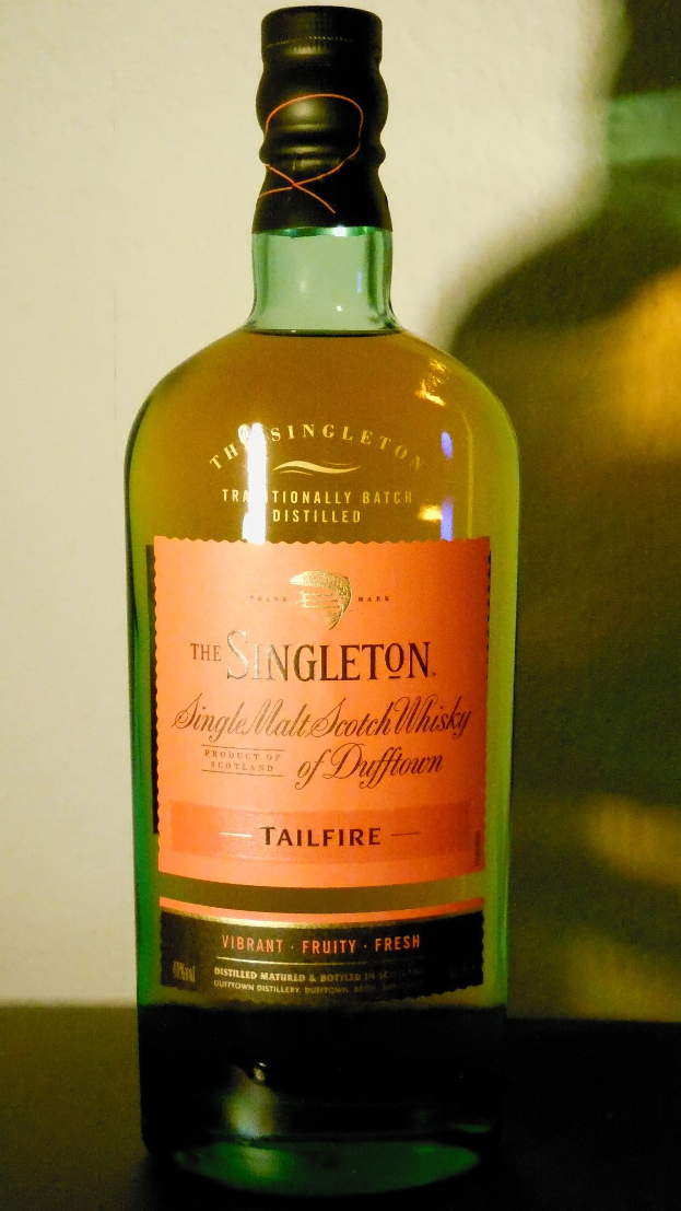 Eine tiefe bernsteinfarbene Flasche Singleton of Dufftown Tailfire Single Malt Scotch Whisky mit einem schwarzen Etikett, das den Namen und ein Wappen mit einem Löwen und einer Burg zeigt.