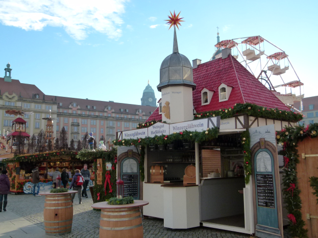 Ein geschäftiger Weihnachtsmarkt in Nürnberg, Deutschland mit Menschen um geschmückte Stände, festlicher Beleuchtung, Schmuck, Gebäuden, einem Riesenrad und einem bewölkten Himmel, mit einer Tafel mit Text auf der rechten Seite.
